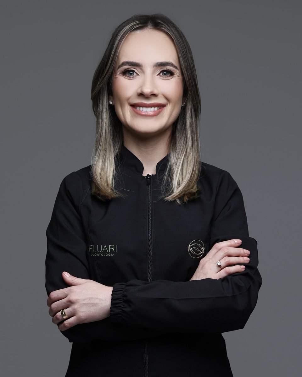 Dra. Rafaela Pagliosa Winter, cirurgiã-dentista que faz implantes na Fluari Odontologia em Lages/SC, de jaleco preto e braços cruzados